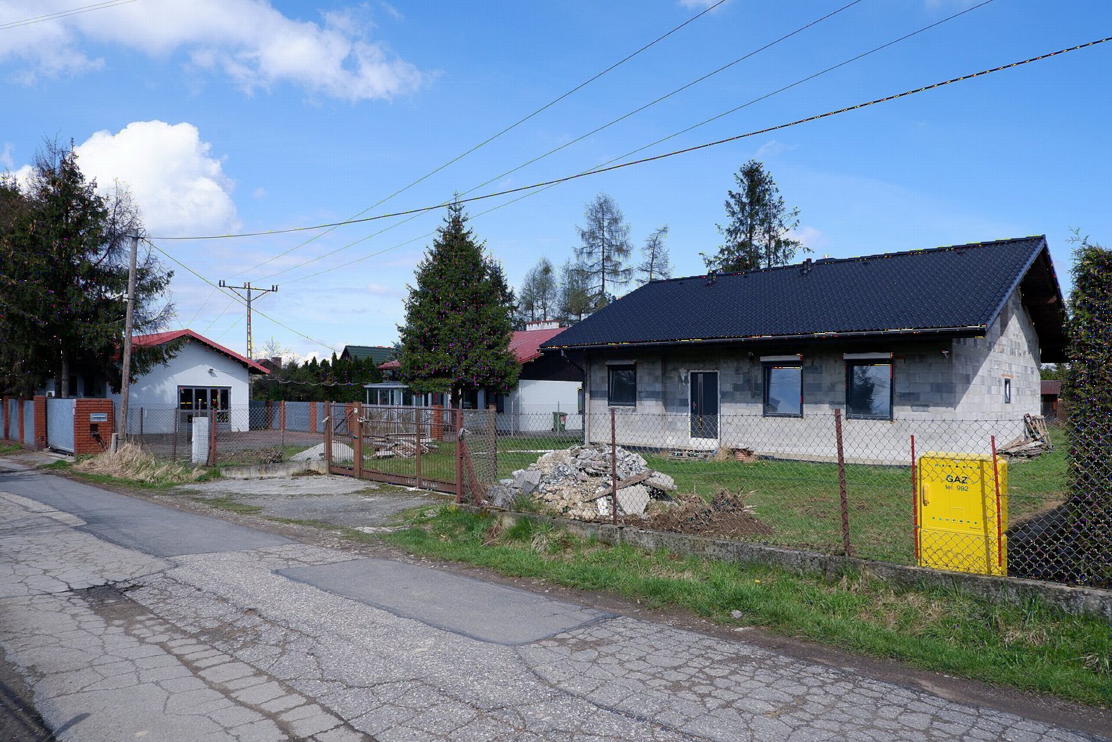 Nowy parterowy dom jednorodzinny w stanie surowym zamkniętym obok starszych domów przy osiedlowej ulicy