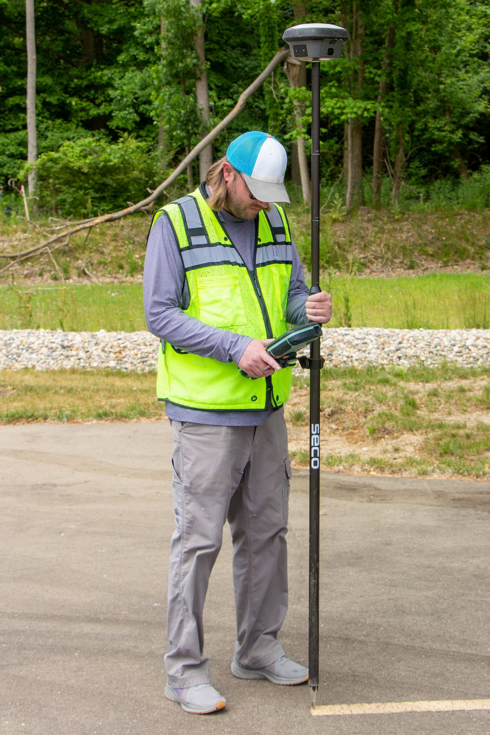 Geodeta w kamizelce odblaskowej wykonuje pomiar tyczką z odbiornikiem satelitarnym GNSS